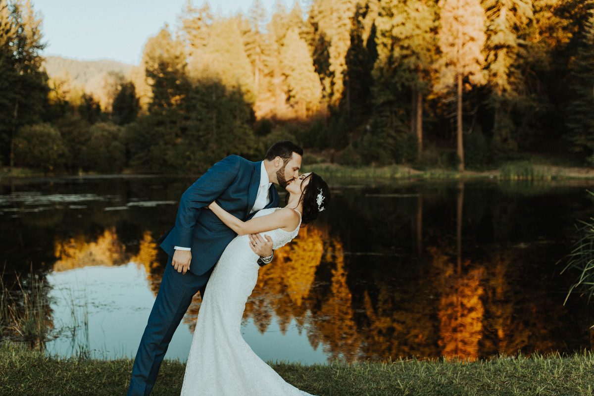 A wedding couple with the groom kissing the bride in front of the Greenhorn Ranch pond at sunset.