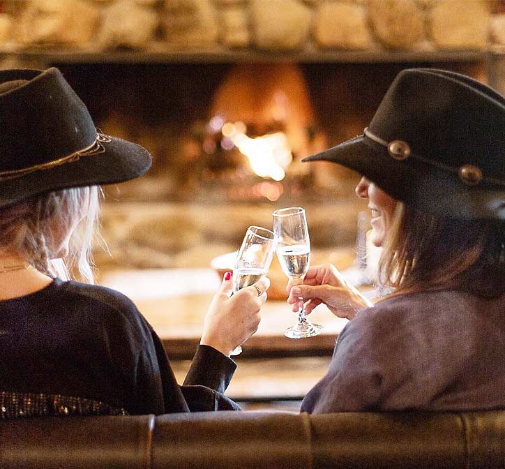 Two friends toasting champagne flutes in front of the fire in the Lodge at Greenhorn Ranch