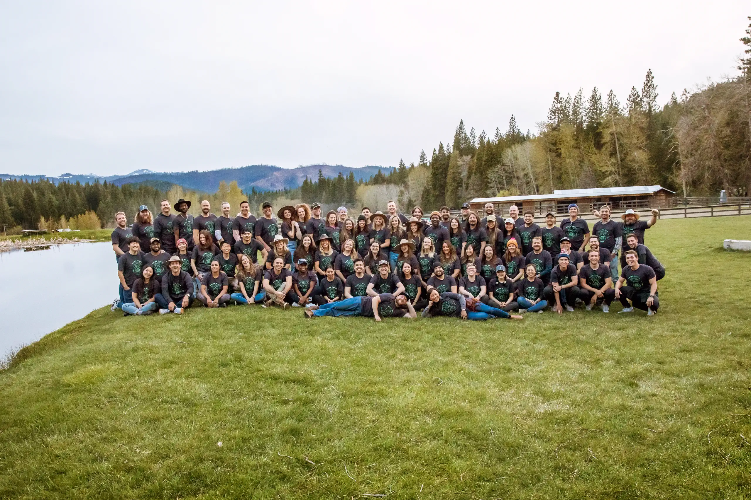 A group standing on green grassholding a big metal Greenhorn Ranch sign with pine trees behind them